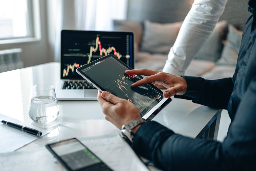 Two professionals using a tablet and laptop to analyze market trends in a modern office setting.